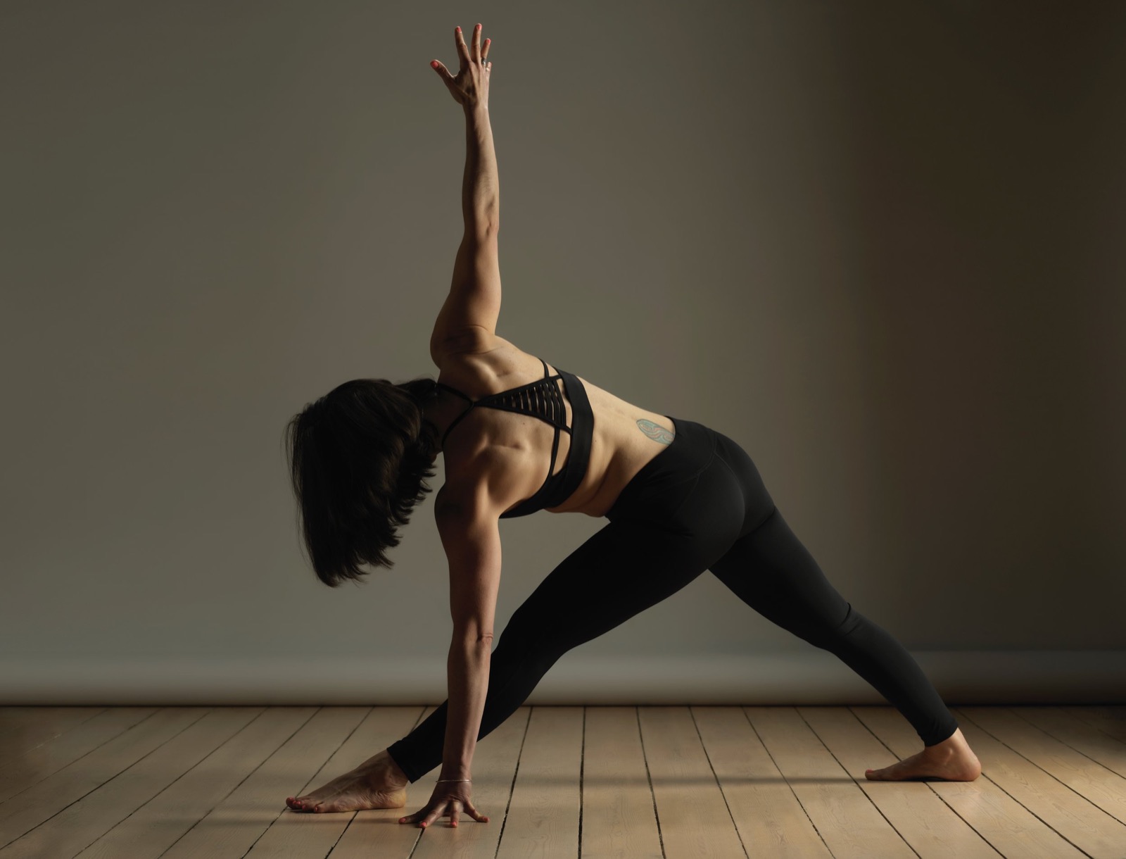 Xenia in a wide standing pose, one arm reaching to the ceiling, on a wooden floor